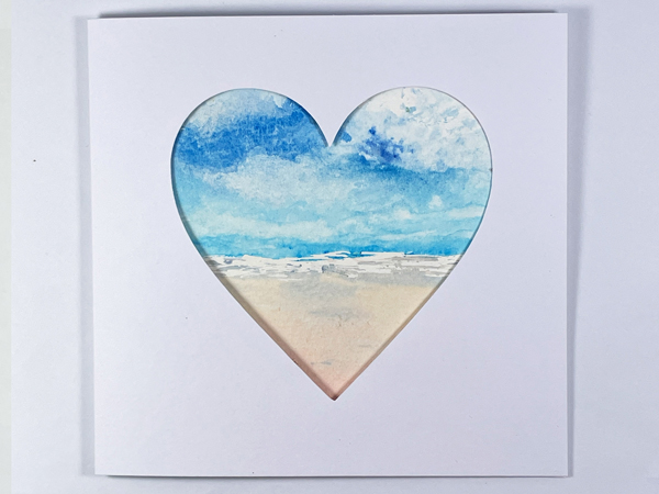 Beach set inside a square card with a heart aperture