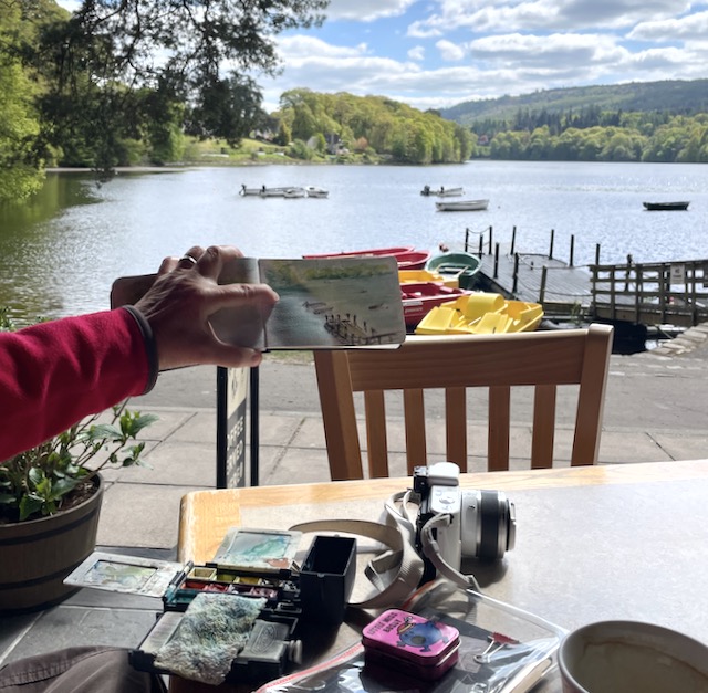Jane holding sketch of Pitlochry Boating Station, with painting equipment on table